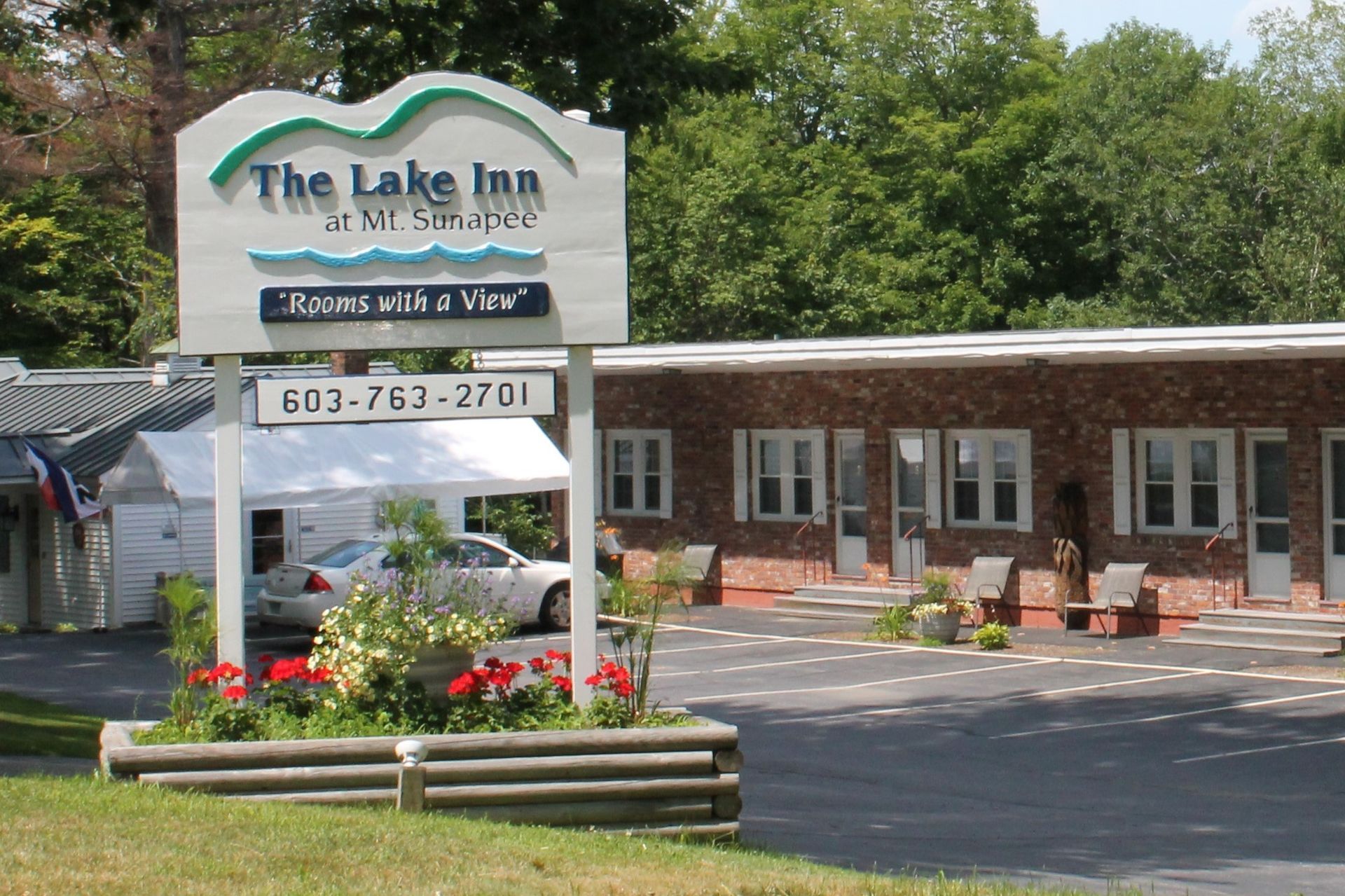 The Lake Inn at Mt. Sypes sign with a motel building in the background, with a white tent and car.