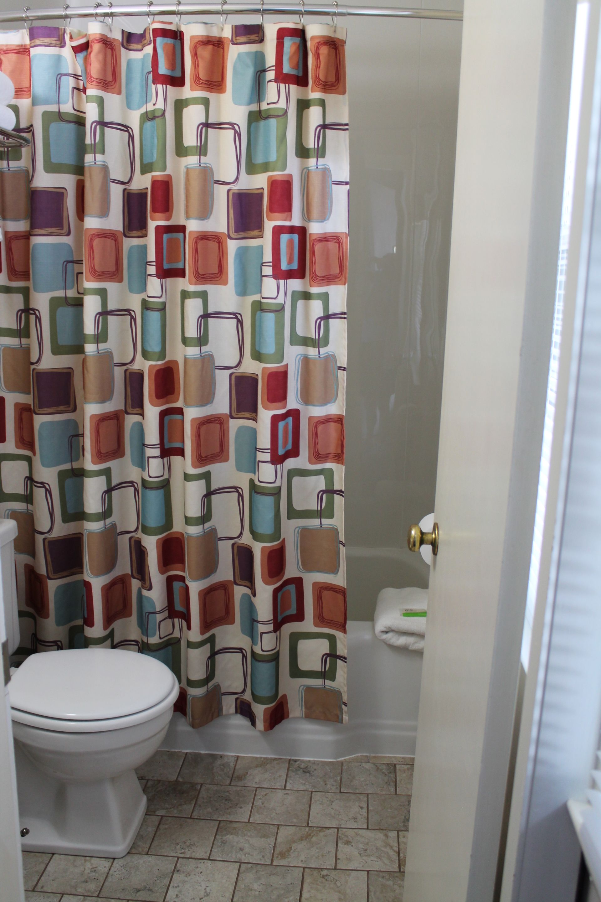 Bathroom with a closed shower curtain patterned with colorful rectangles. A toilet is in the foreground, visible through the doorway.
