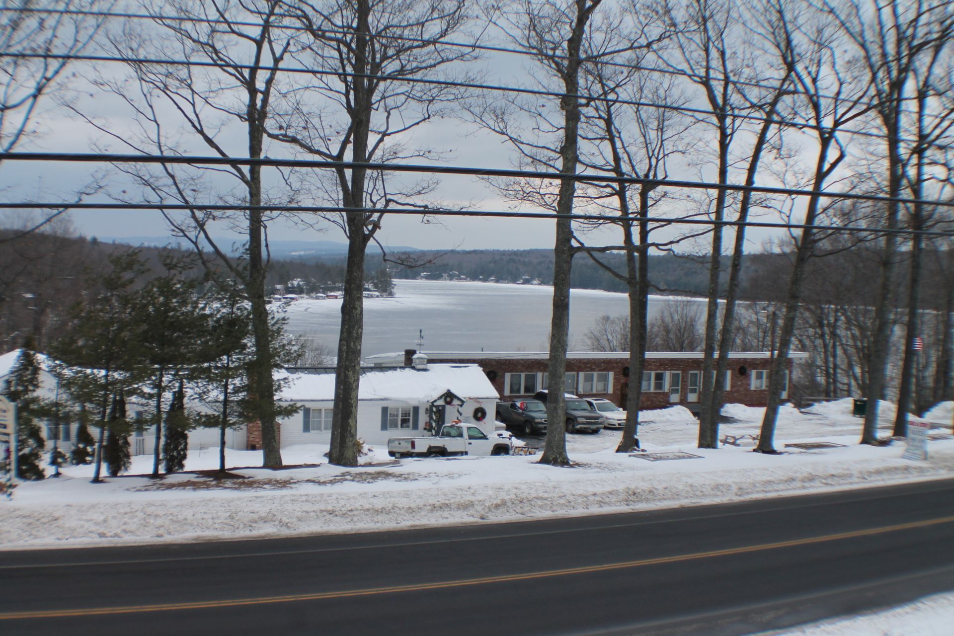 Snowy landscape with a lake in the background, a road in the foreground, and a small motel and trees in between.