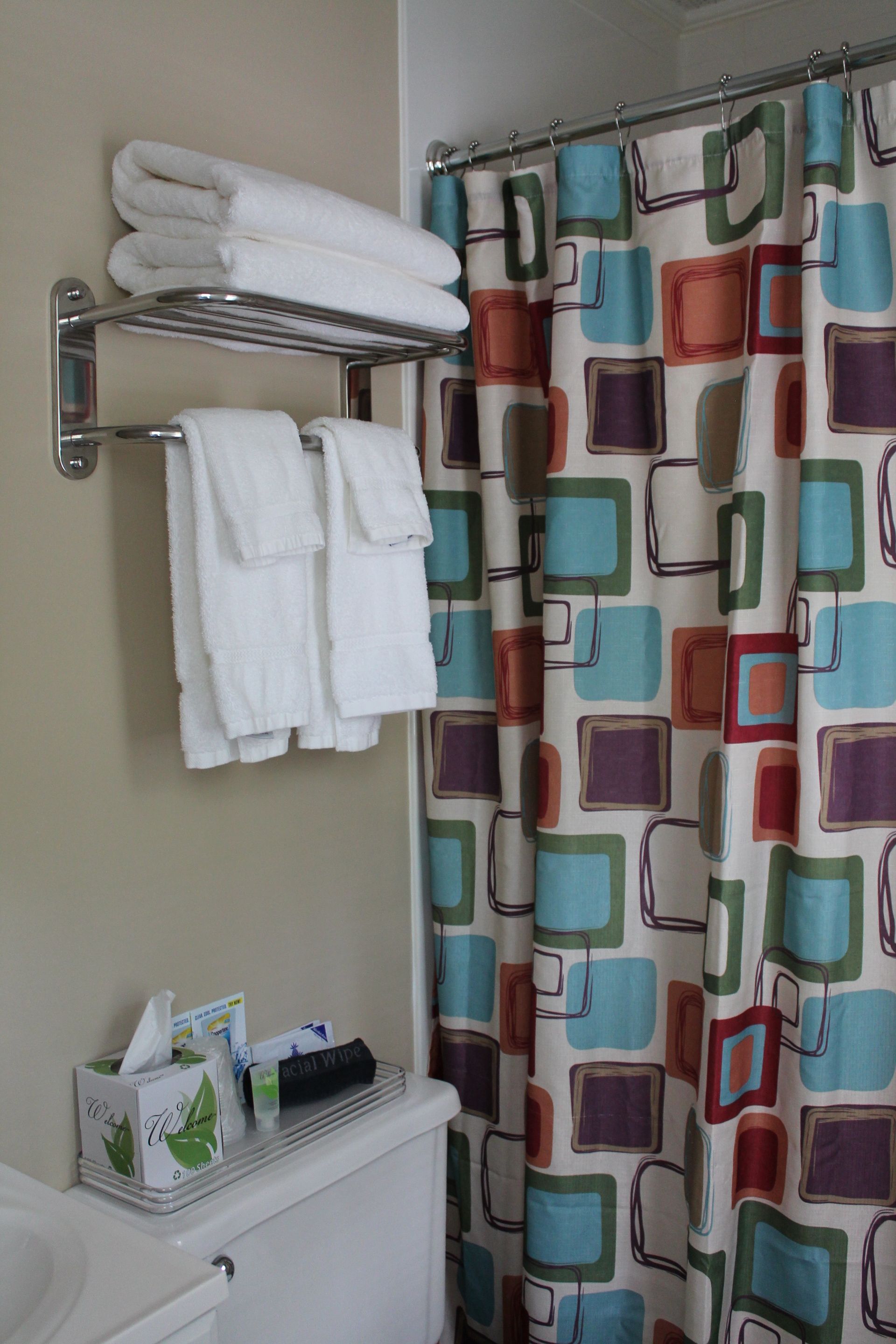 Bathroom with white towels on a rack, a toilet, and a colorful shower curtain with squares.