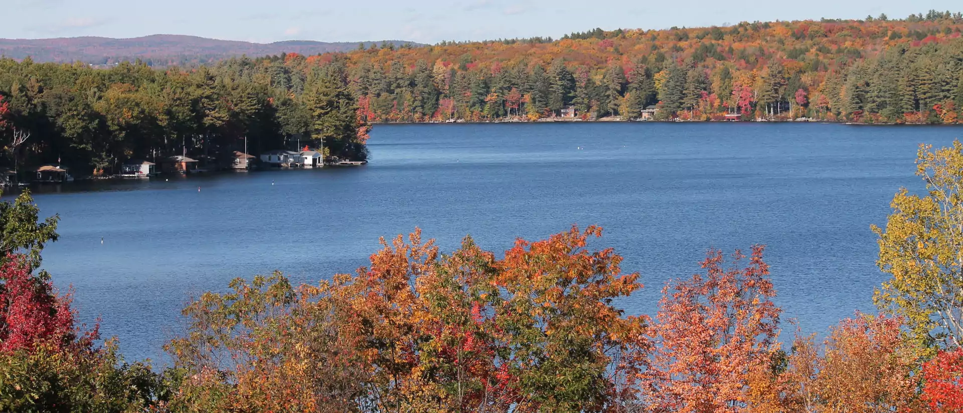 A scenic lake surrounded by trees with fall foliage. Calm blue water reflects the surrounding autumn colors and clear sky.