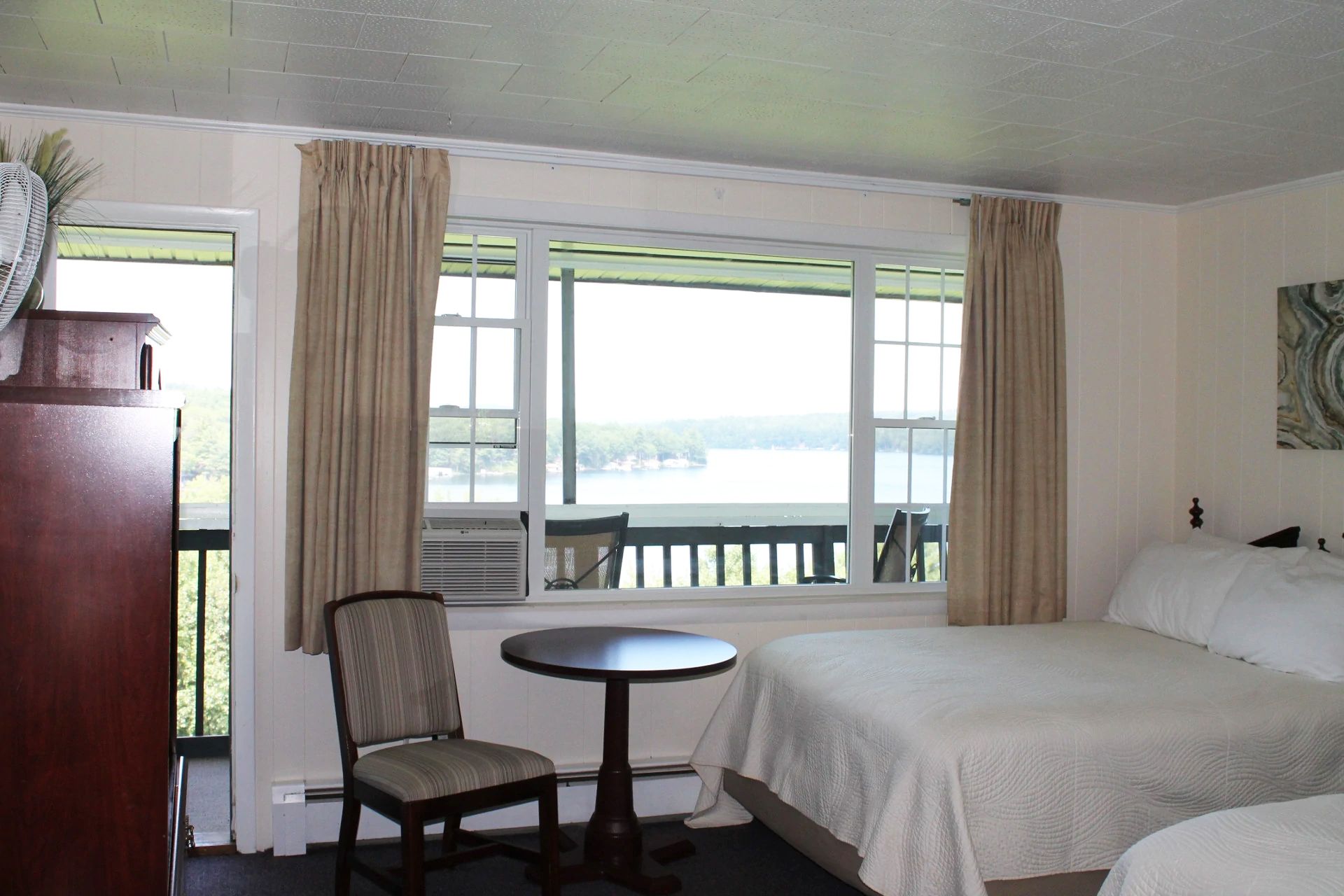 Premium Double Balcony Room with two beds, a small table and chair, a window overlooking a lake, and a balcony.