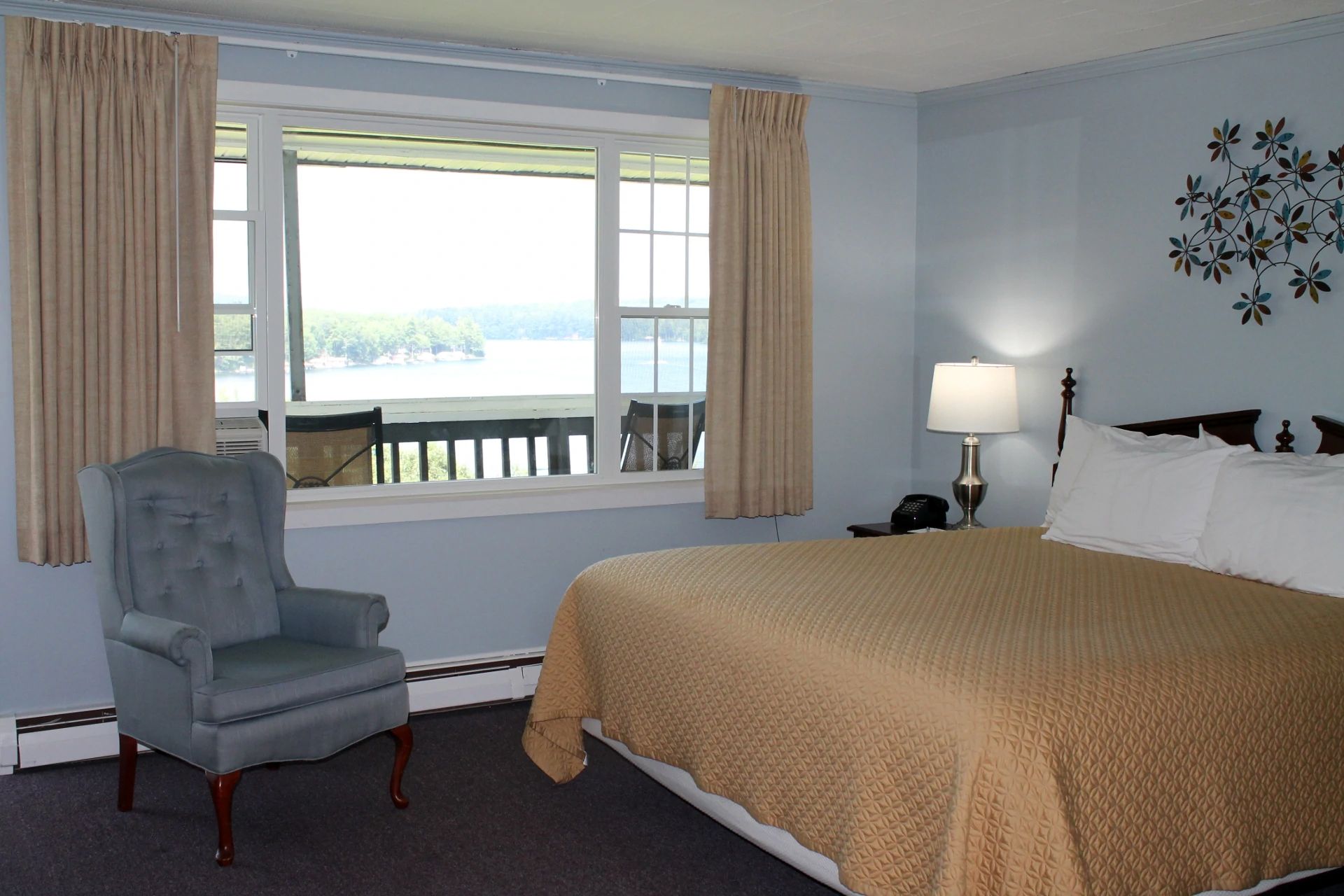 Premium King Balcony Room bed covered in a gold quilt, a blue armchair, and a large window with a view of a body of water.
