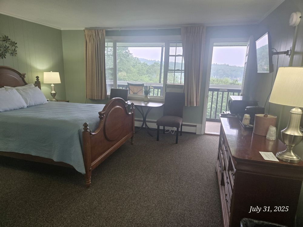 Premium Queen Anne Balcony Room with a dresser, TV, and an open door to a porch. Pale green walls and dark furniture.