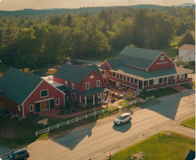 Aerial view of the NL Barn building complex with a white SUV driving on a road in front. Trees surround the buildings.