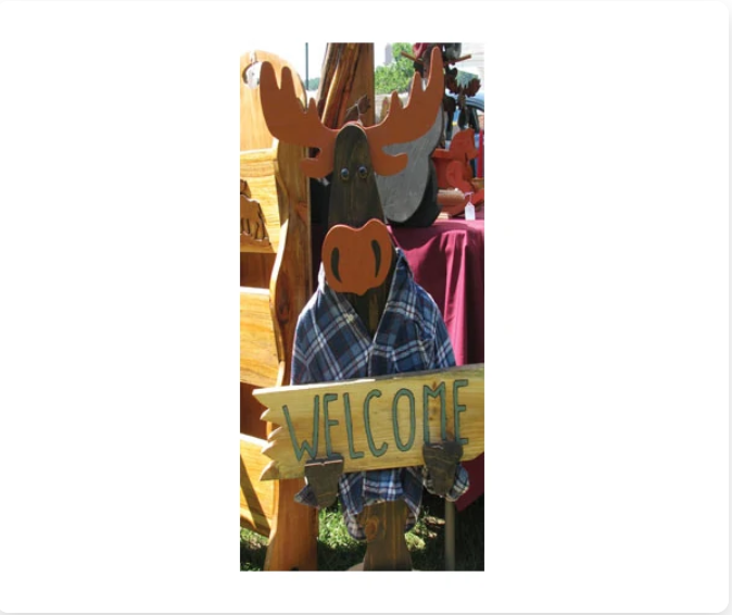Wooden moose sculpture wearing a blue plaid shirt, holding a 