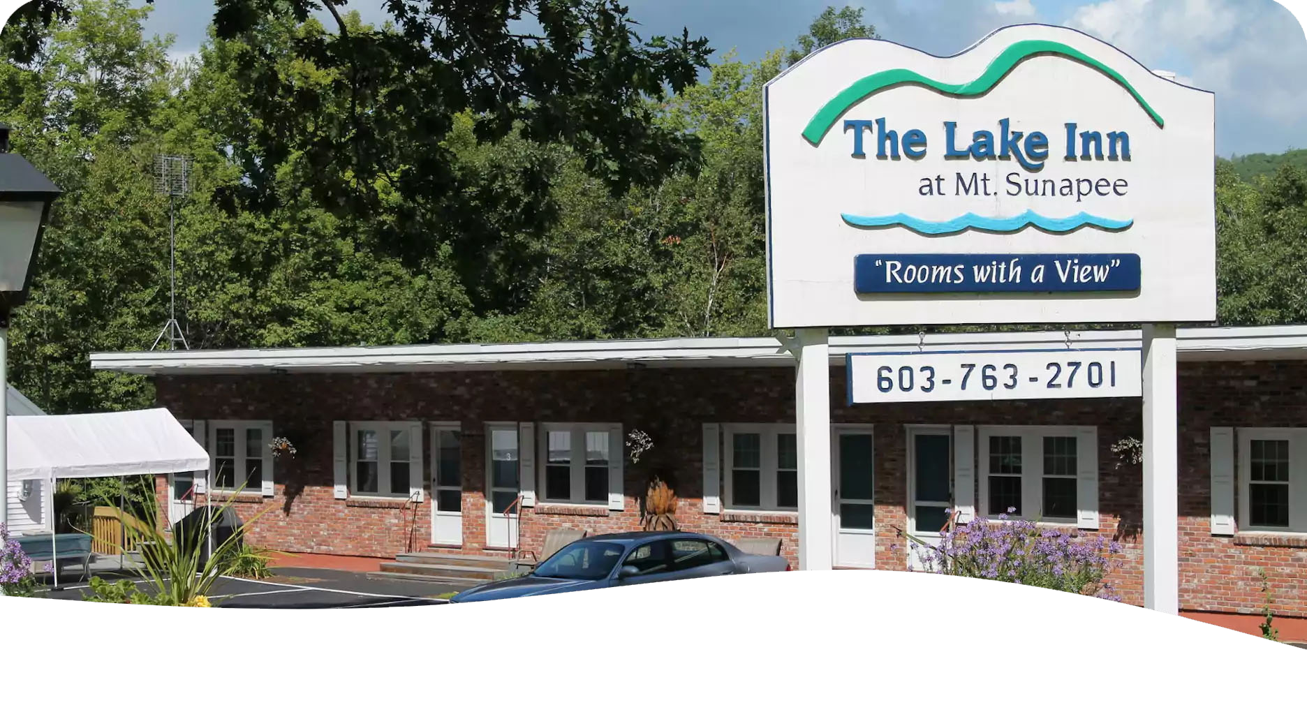 The Lake Inn at Sunapee motel exterior with sign, brick facade, and car parked out front.