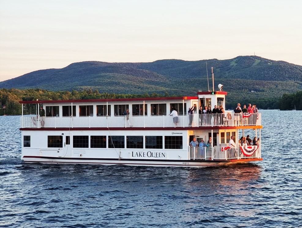 Paddle boat on a lake with passengers, mountains in the background.