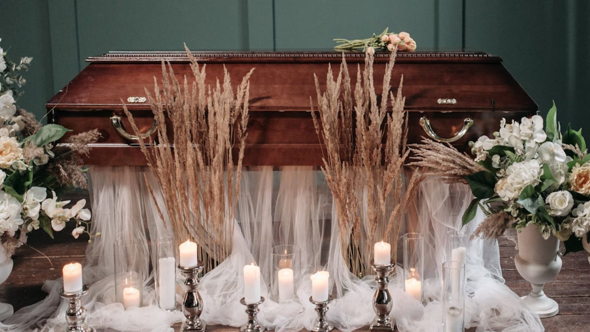 Un ataúd de madera, situado en el centro de un escenario, estaba adornado con espigas de trigo, cubierto con tela blanca y con velas encendidas en un entorno floral.