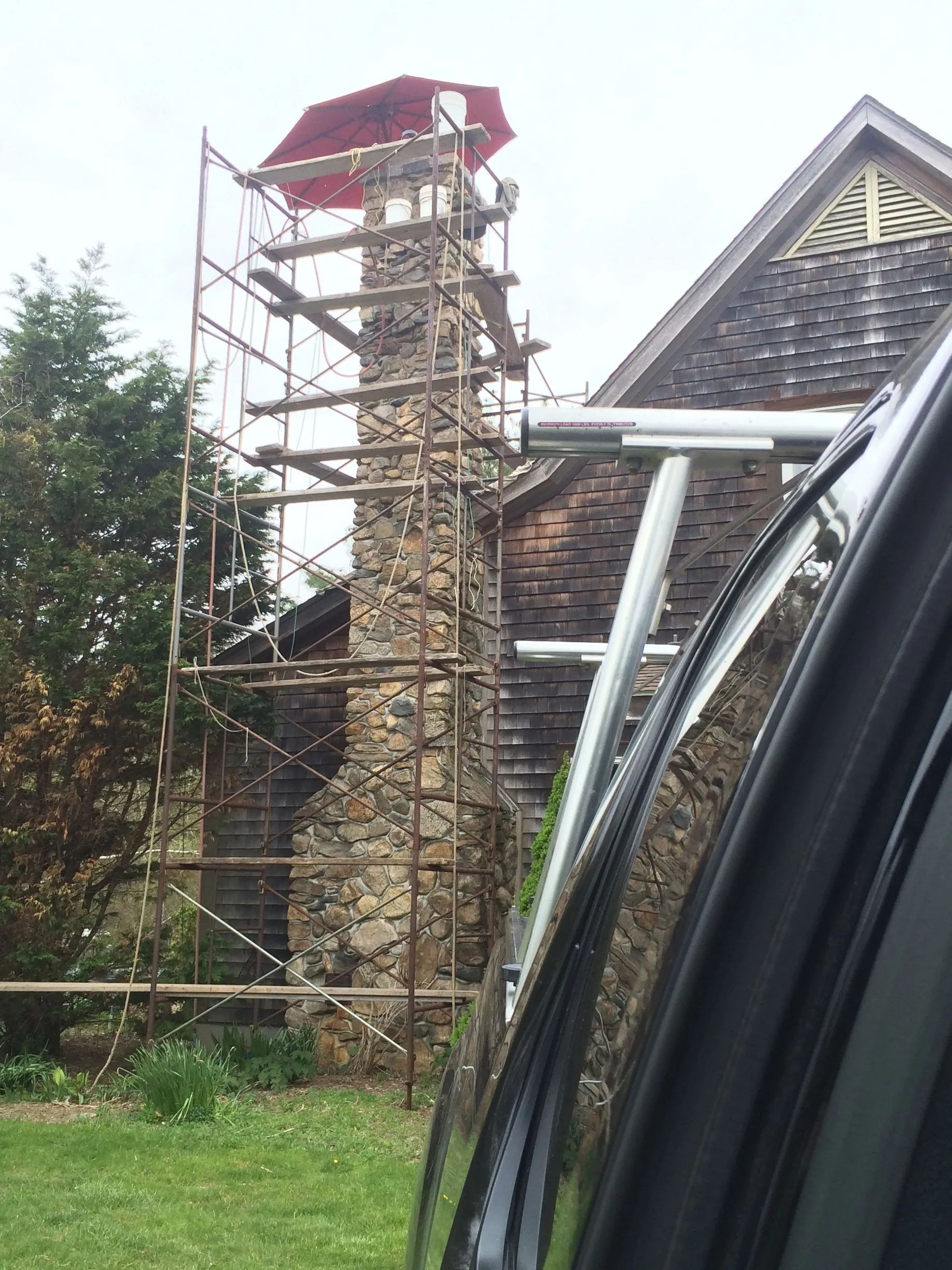 A car is parked in front of a stone chimney with scaffolding around it.