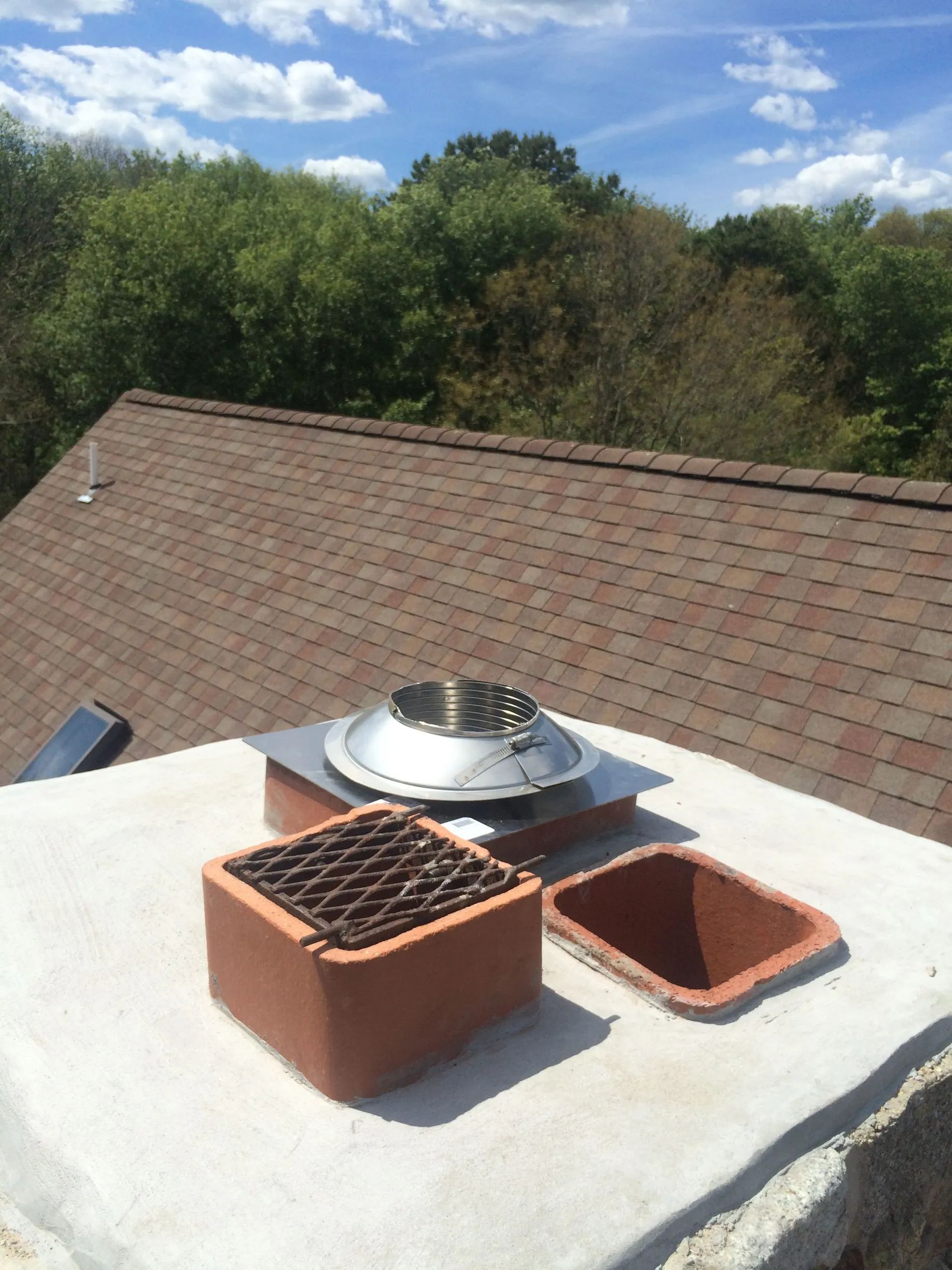 A chimney on top of a roof with trees in the background.