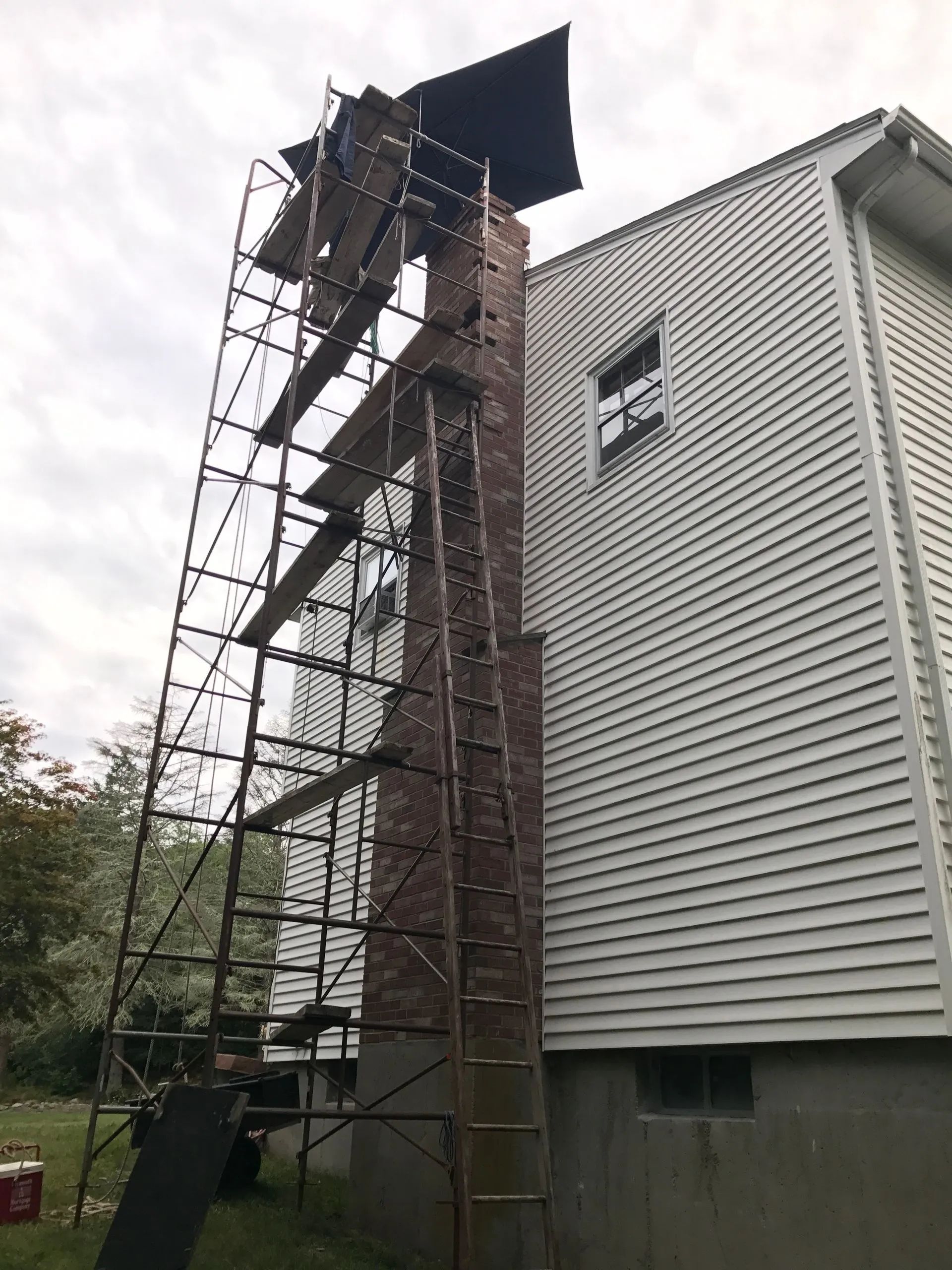 A scaffolding is being used to repair a chimney on the side of a house.