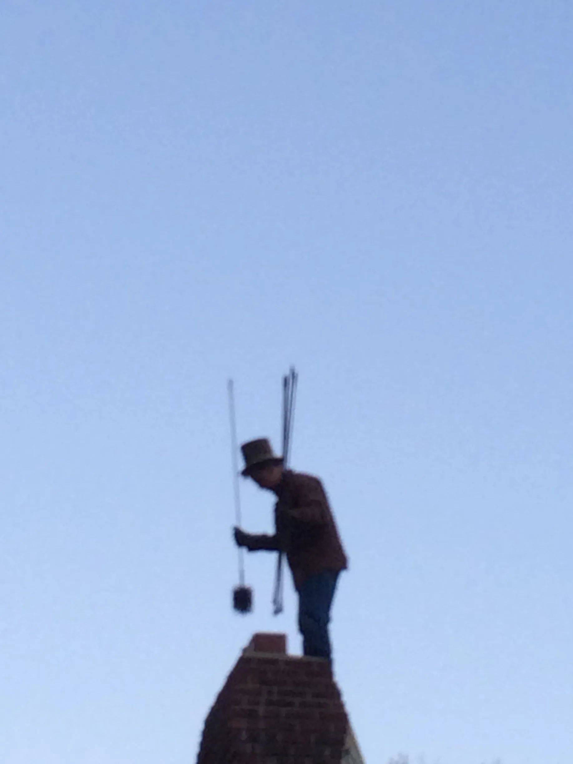 A man is standing on top of a chimney holding a brush.