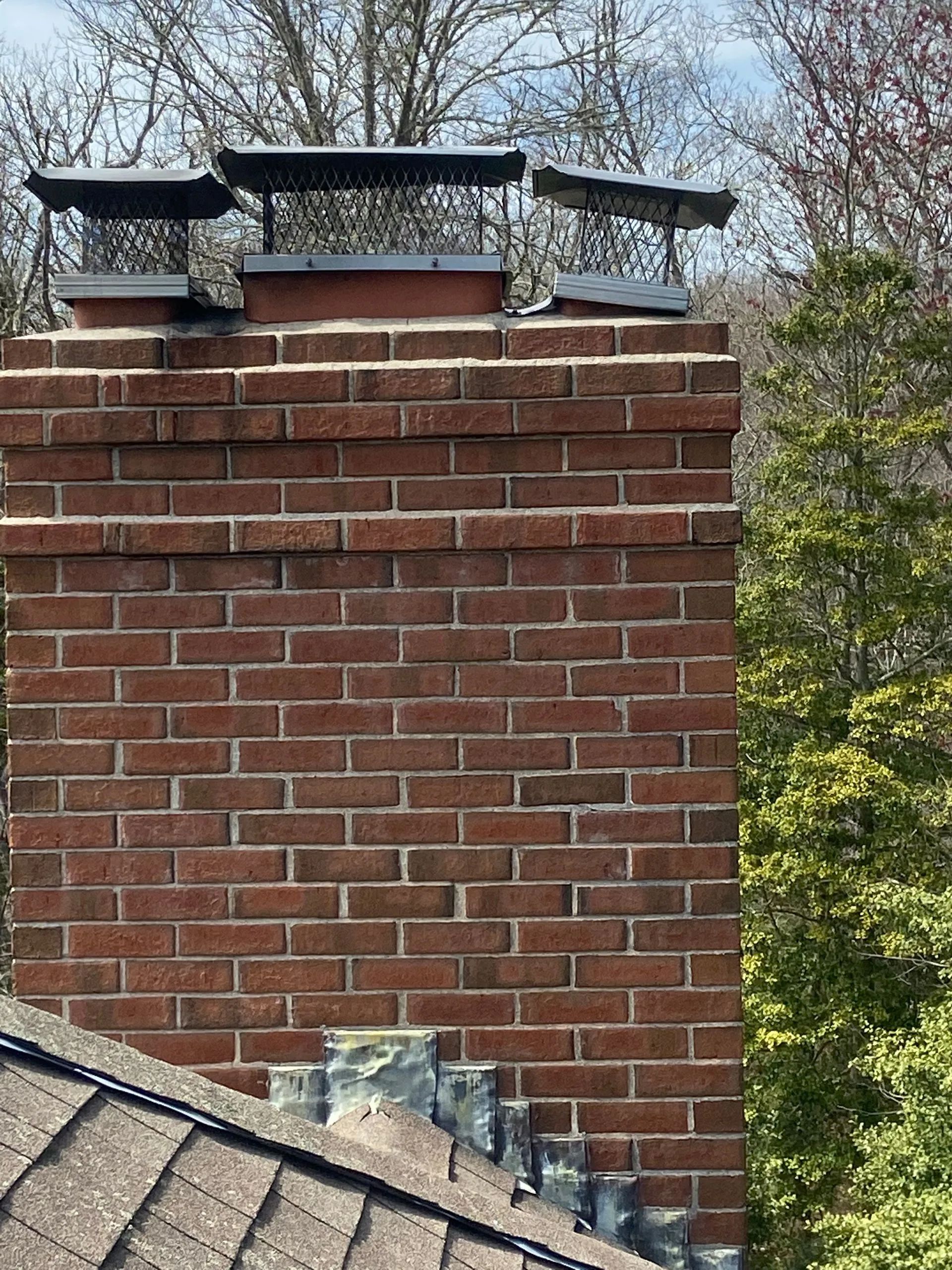 A brick chimney on top of a roof with trees in the background.