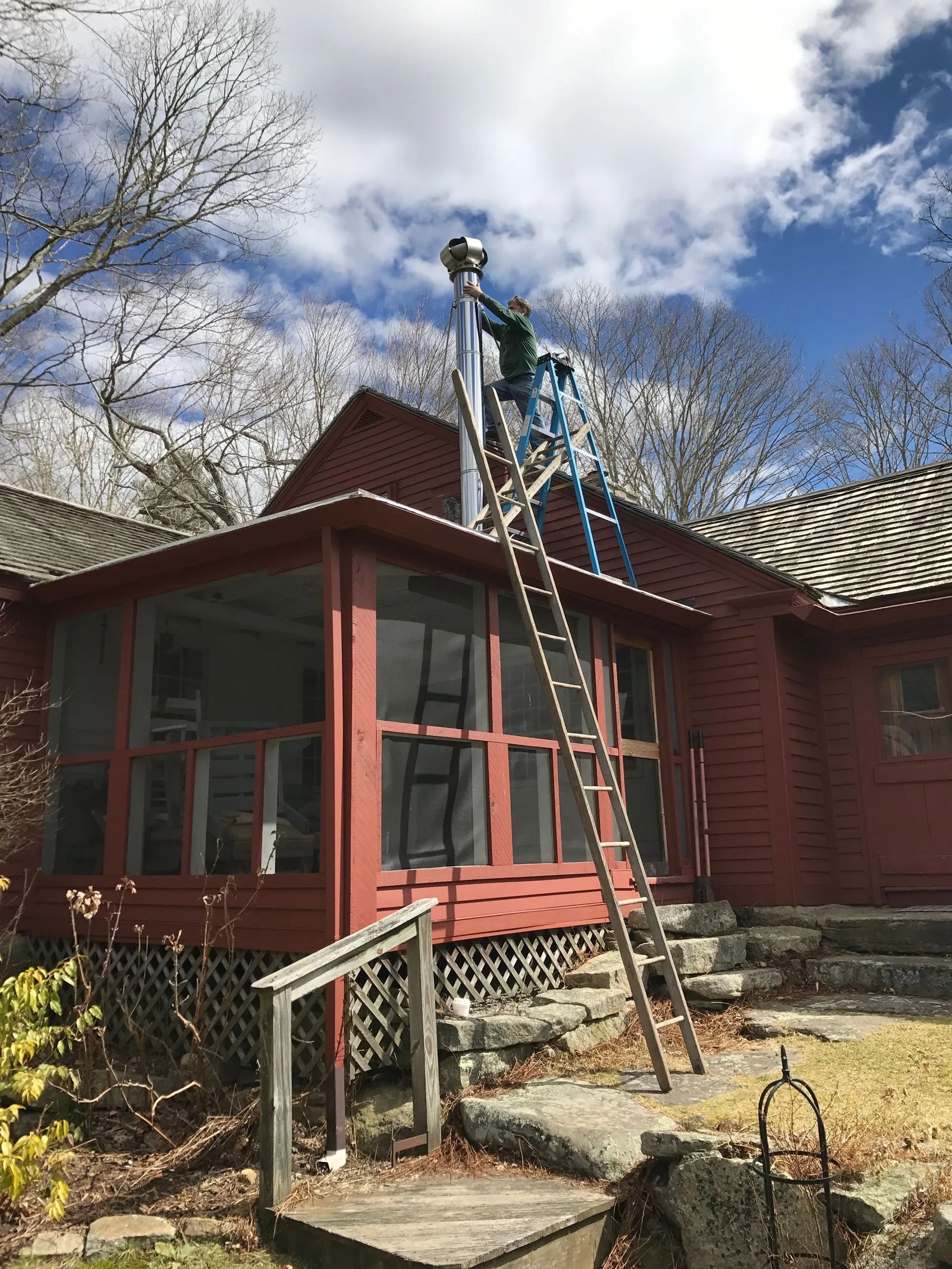 A man is standing on a ladder in front of a red house.