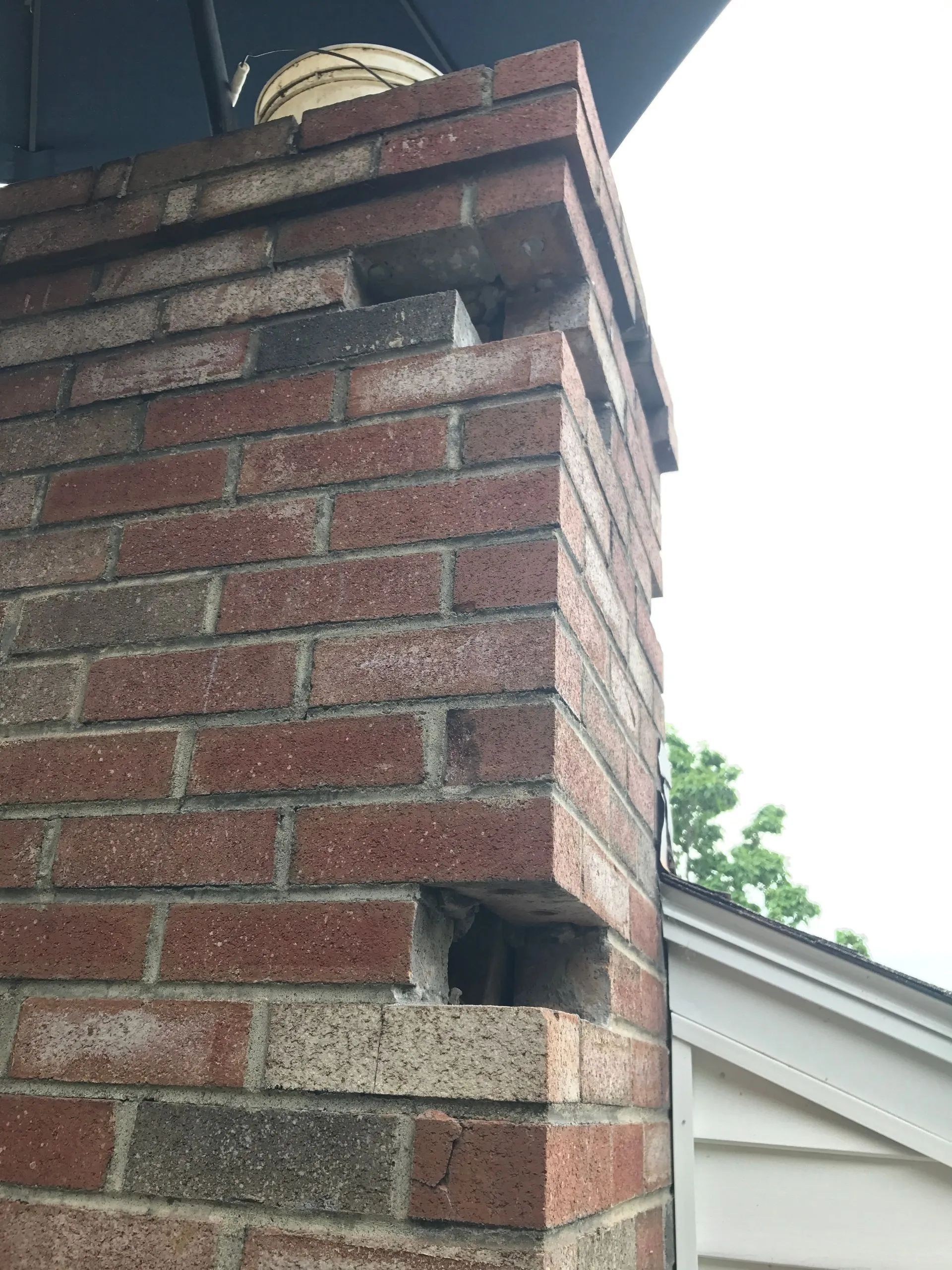 A brick chimney with a hole in it and a bucket on top of it.