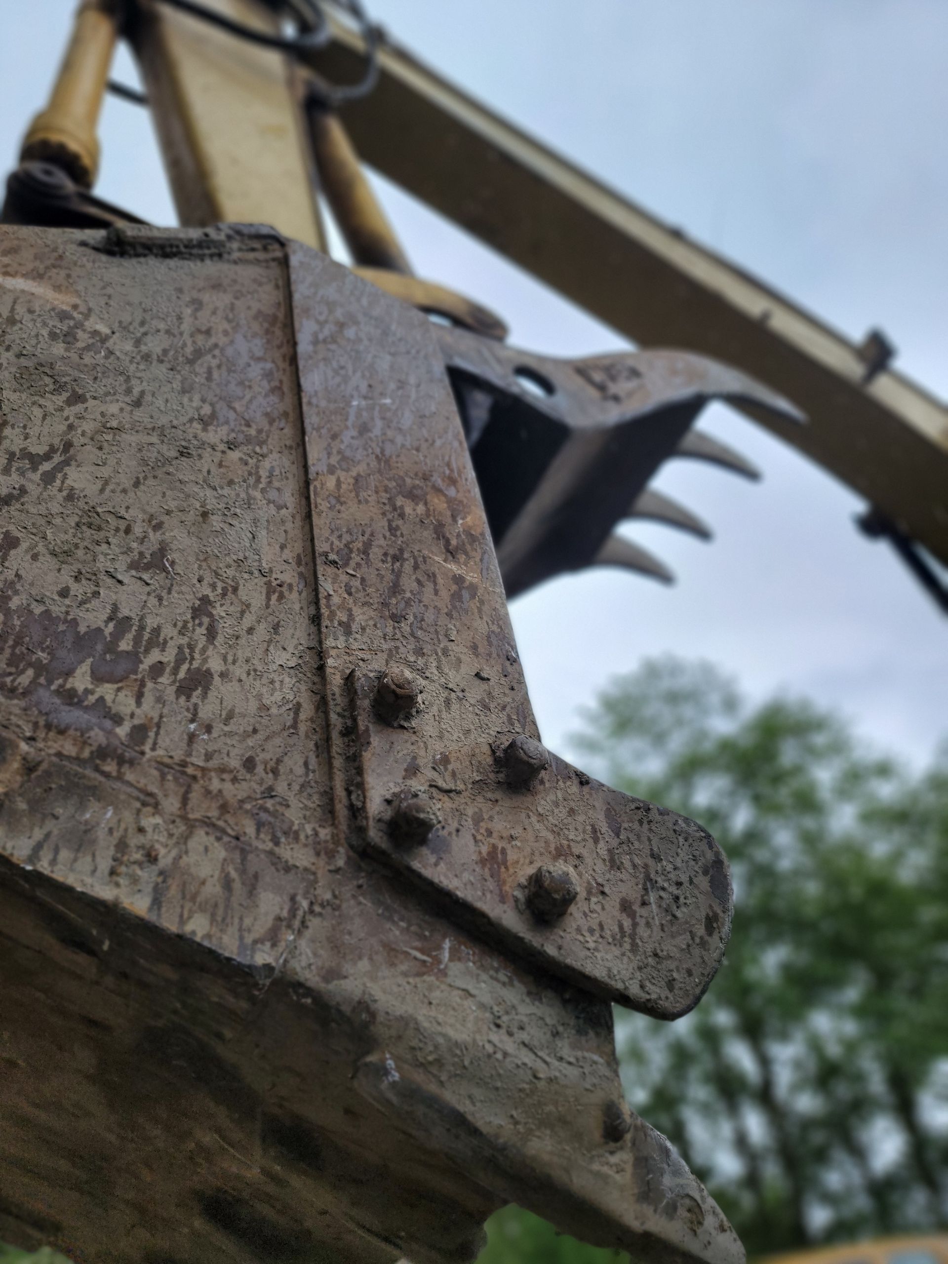 Close-up of a rusty excavator bucket with teeth, in a natural setting.