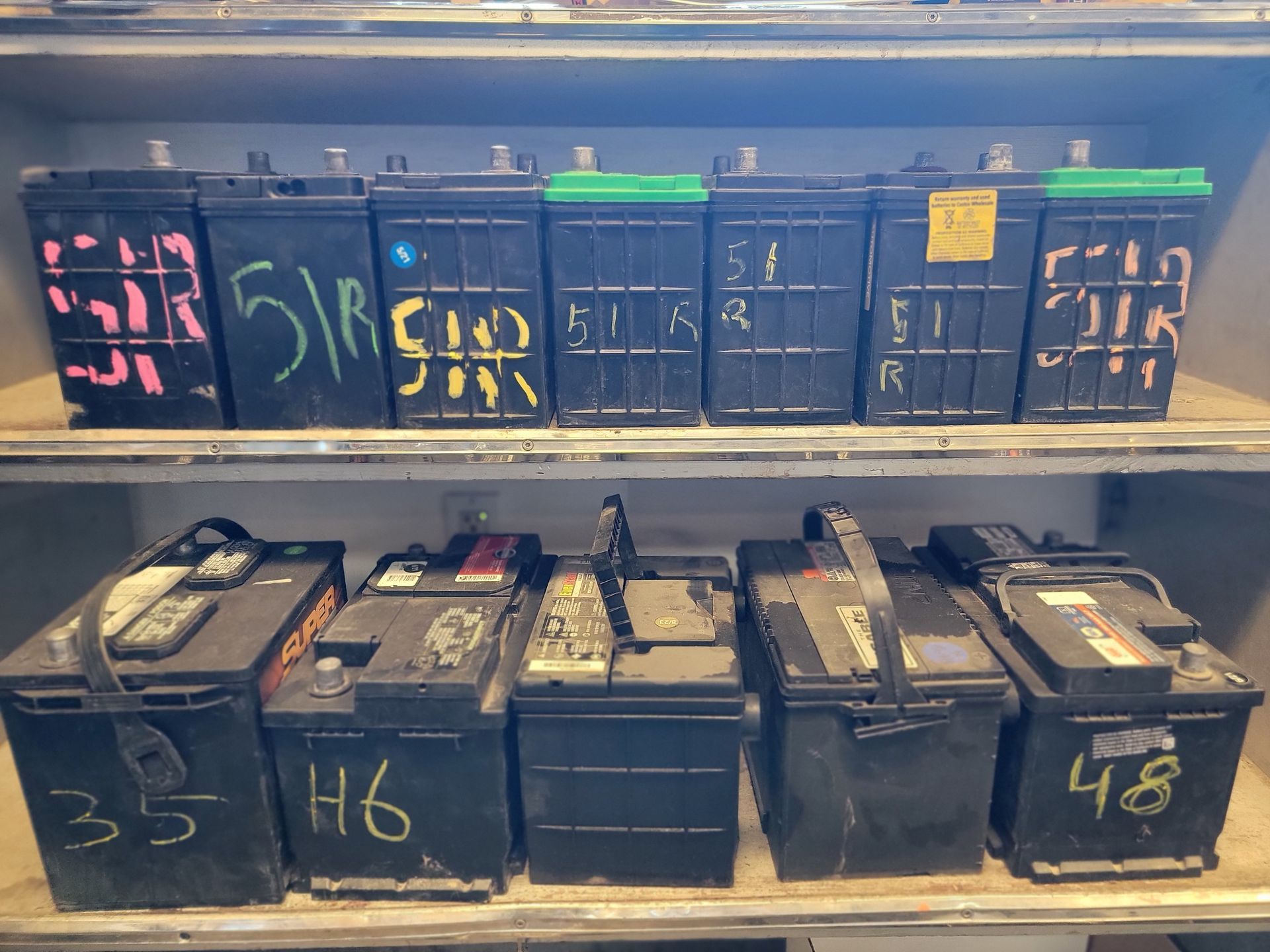 Shelf of black car batteries labeled with numbers and codes.
