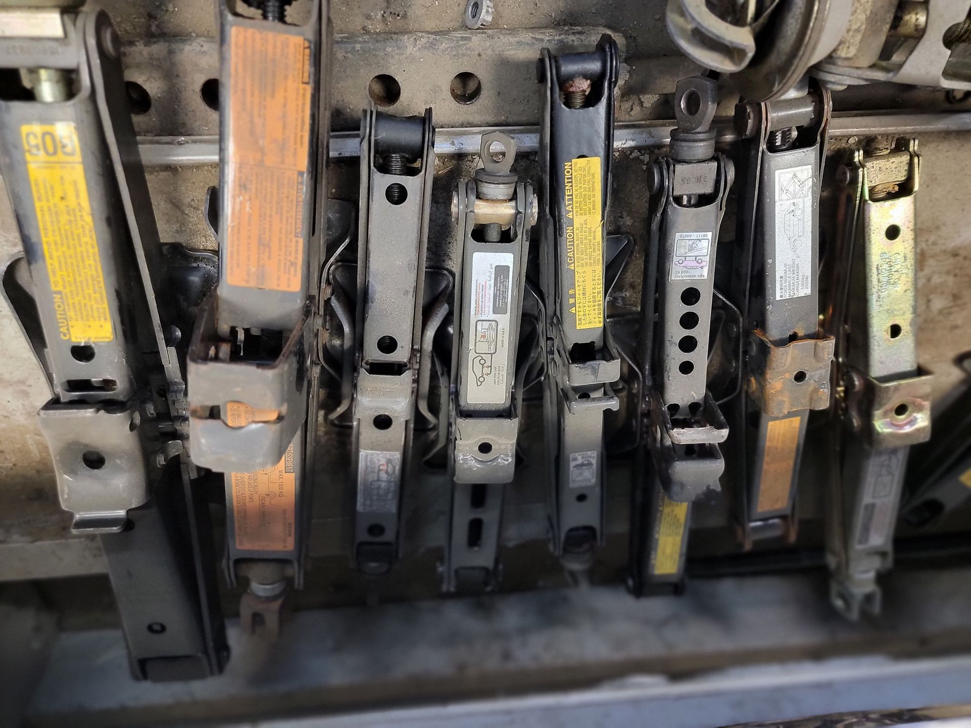 Six vertical jacks with metal and wood components, arranged in a row, likely inside an enclosed cabinet.
