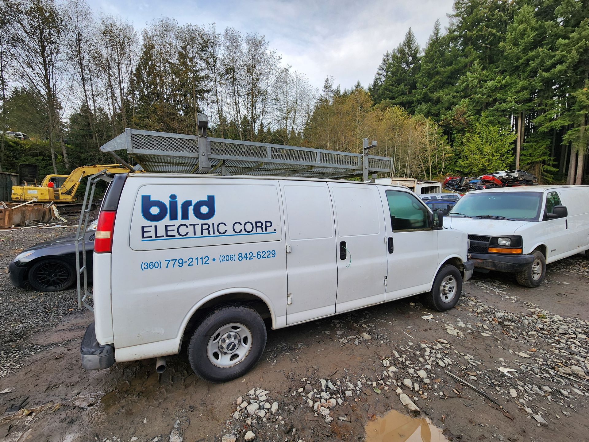 White Bird Electric Corp van with ladder rack, parked in a lot with other vehicles and trees.