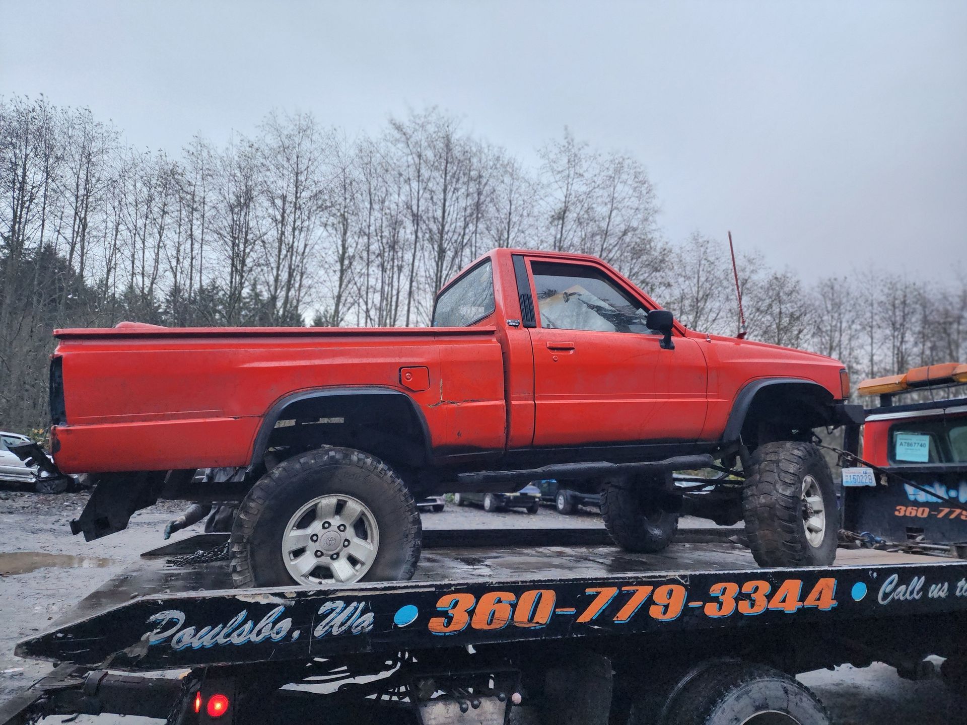 Red Toyota truck on a tow truck in Poulsbo, Washington. The truck is lifted, tires muddy, on a cloudy day.