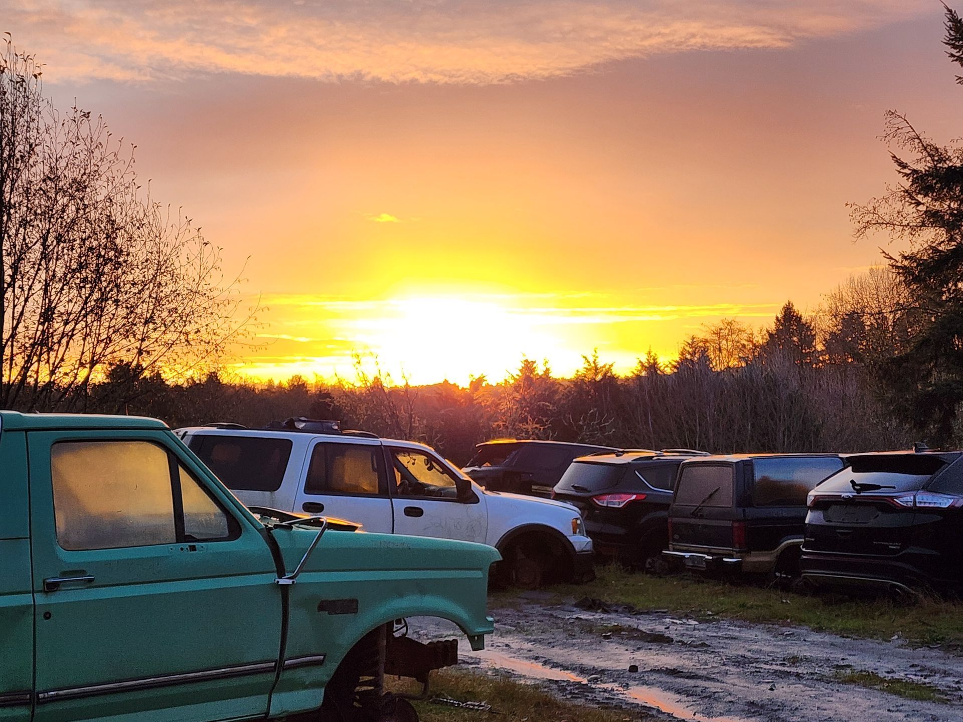 Sunset over a junkyard filled with old vehicles. The sky is orange and yellow.