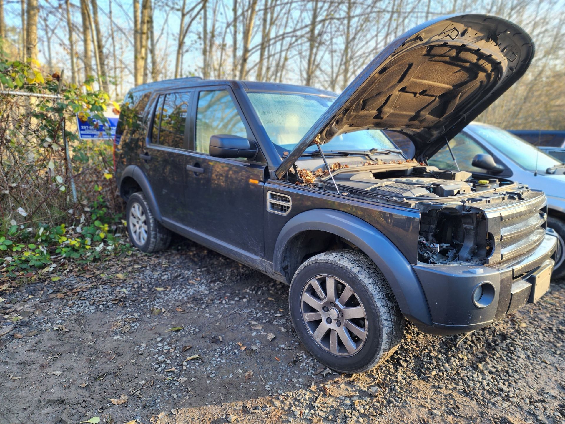 Black Land Rover SUV with open hood, damaged front, parked outdoors.