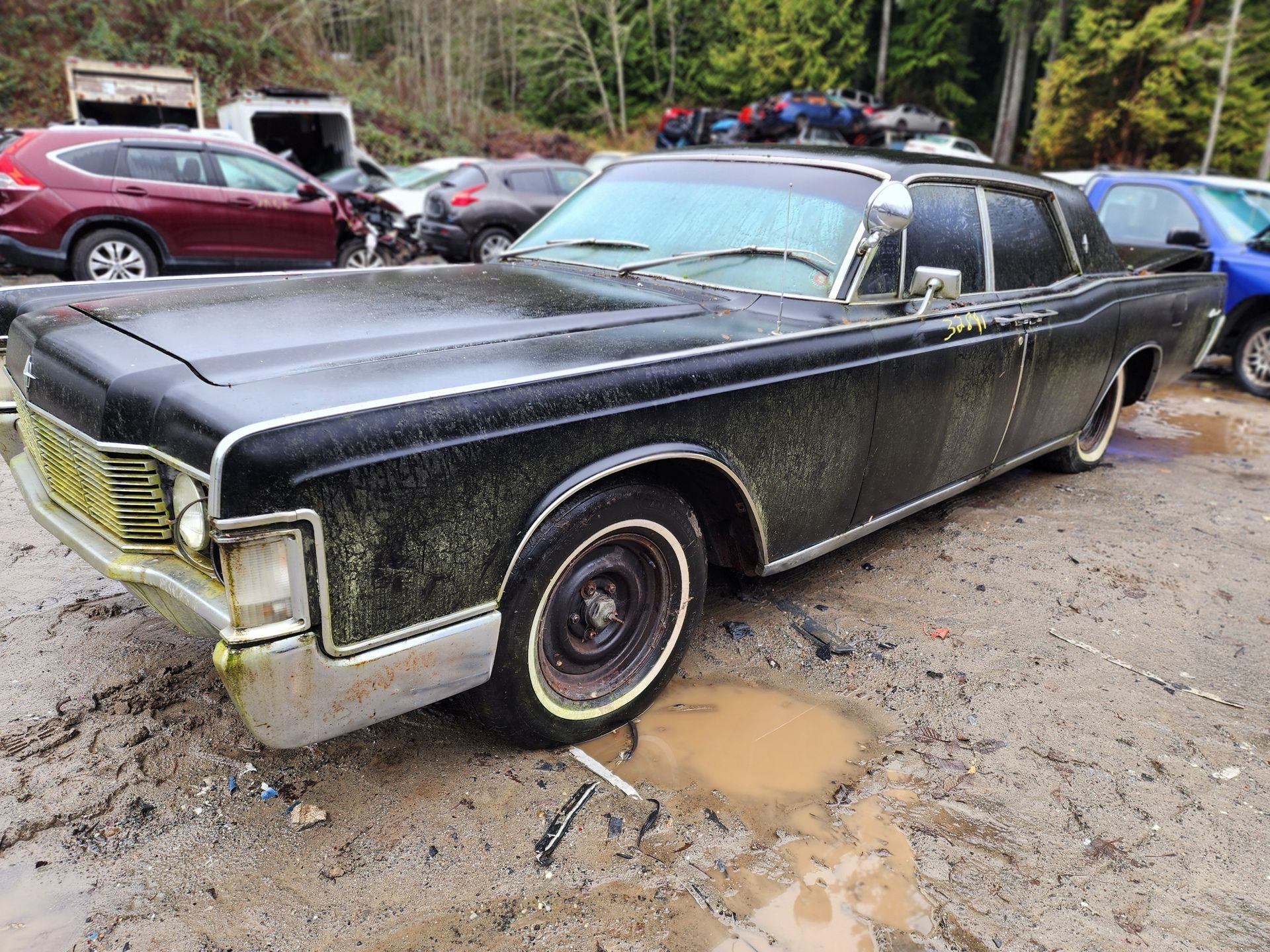 Black Lincoln Continental in a muddy salvage yard.
