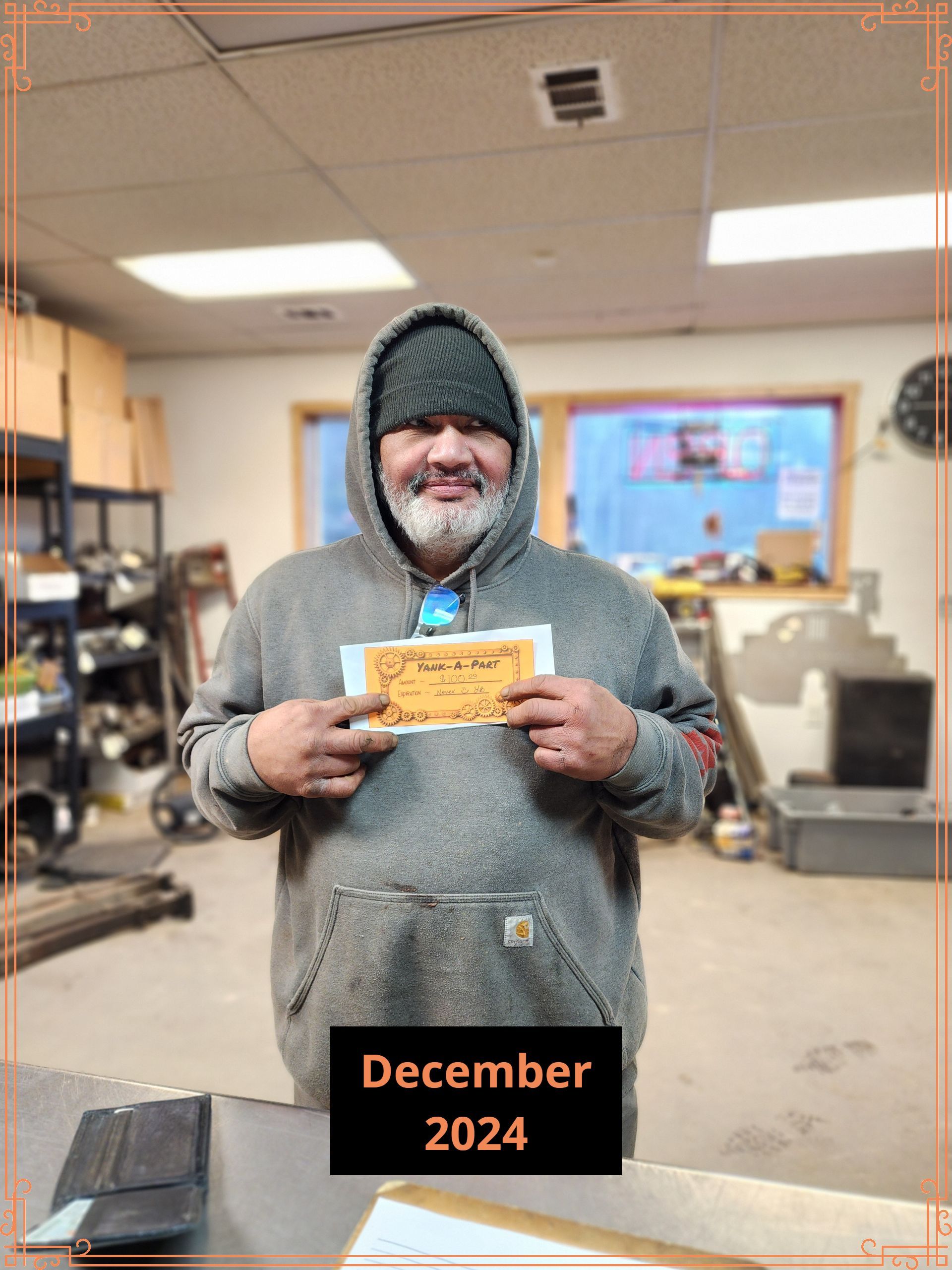 Man in grey hoodie, holding a sign, December 2024, in workshop.