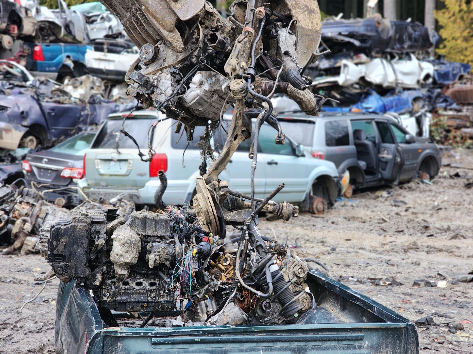 A claw lifting car engines from a junkyard full of discarded vehicles.