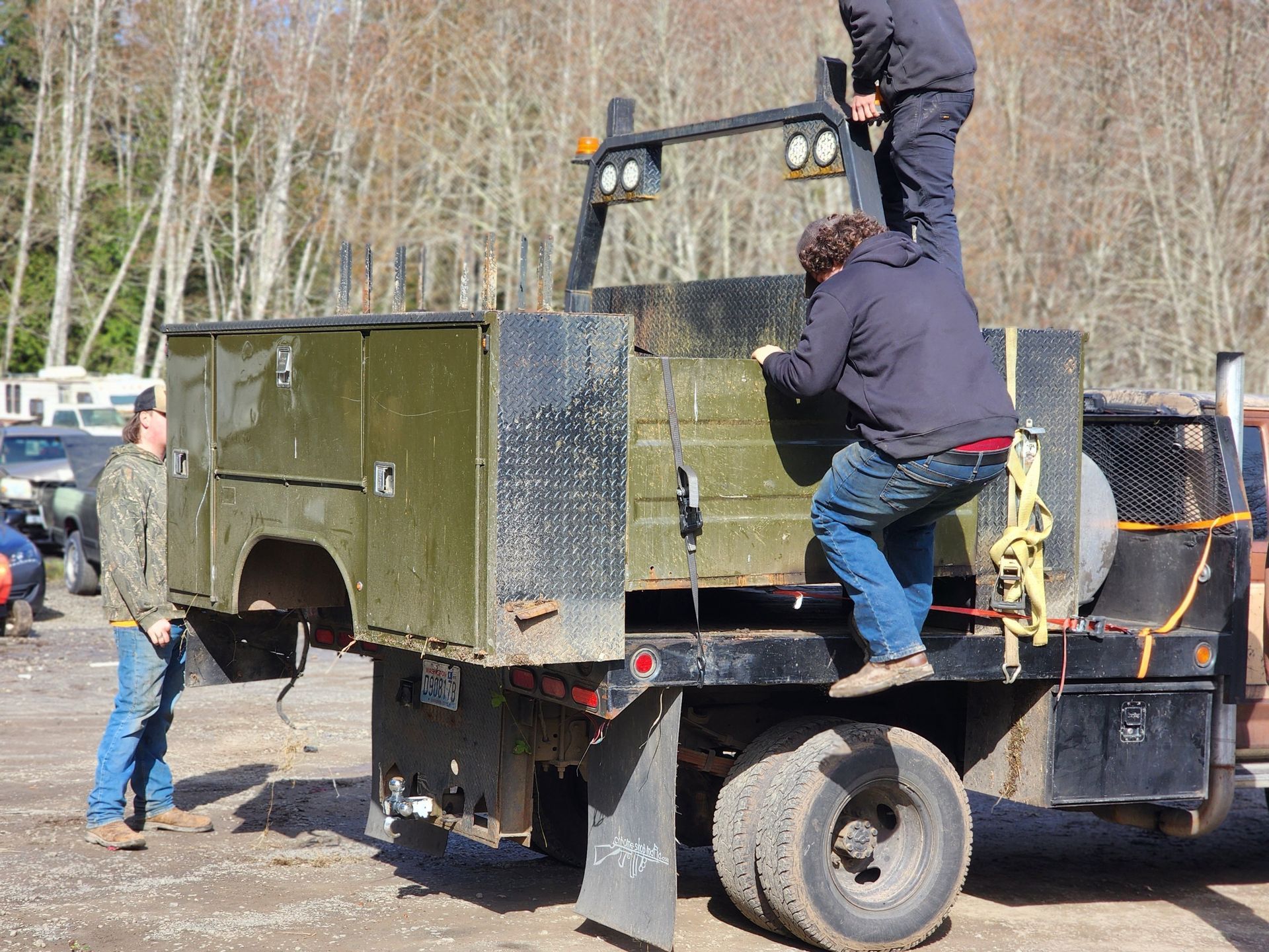 Three people removing a green metal tool box from a flatbed truck in an outdoor setting.