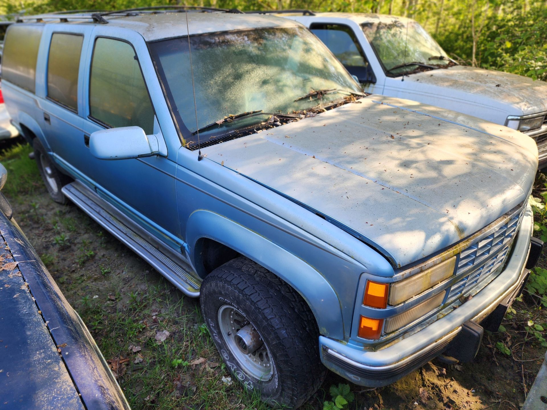 Blue Chevy Suburban in a junkyard, covered in dust.