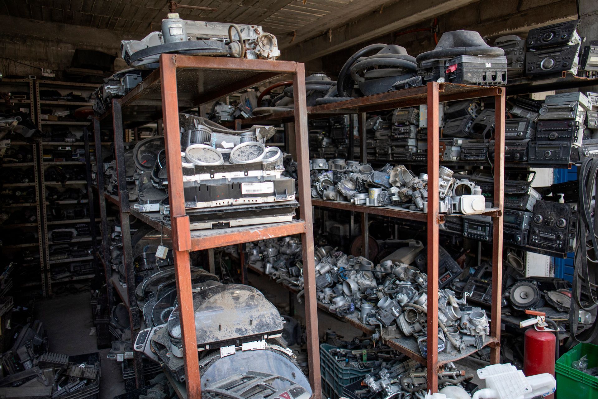 Engine components and dashboards stacked in shelves at a used auto part yard warehouse.