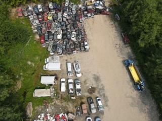 Aerial view of a junkyard with crushed cars and a gravel road in a wooded area.