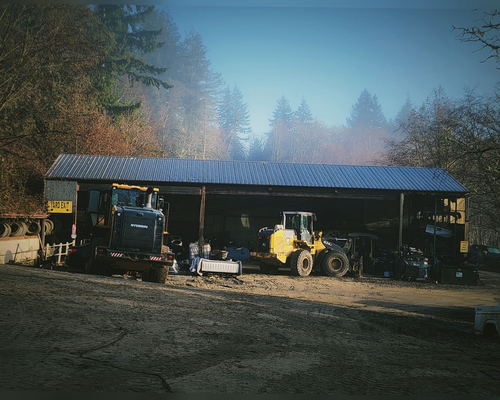 Large open shed with two tractors inside. Overcast day.