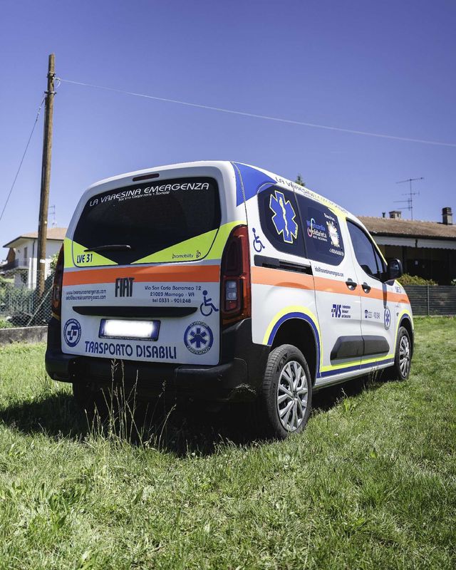 Un furgone ambulanza con segnaletica rossa, gialla e blu è parcheggiato su un campo d'aviazione accanto a un aereo.