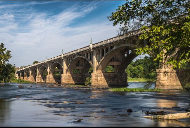 A wooden walkway leading to a gazebo overlooking a body of water at sunset.