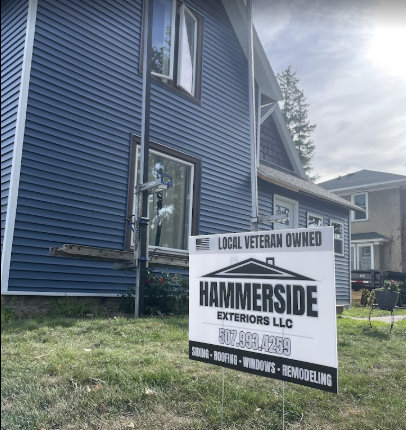 A sign for hammerside exteriors llc is in front of a blue house