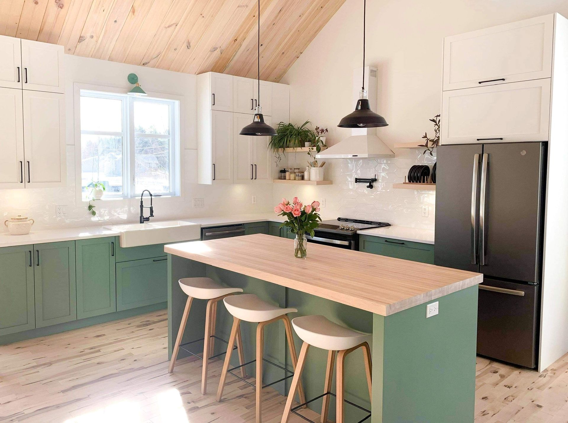Cuisine moderne avec armoires vert sauge, comptoirs blancs et îlot en bois avec tabourets.