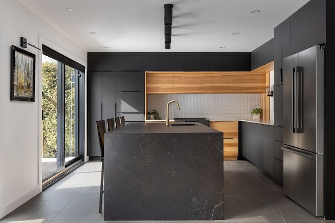 Cuisine moderne avec armoires gris foncé, accents en bois, îlot et réfrigérateur en acier inoxydable.