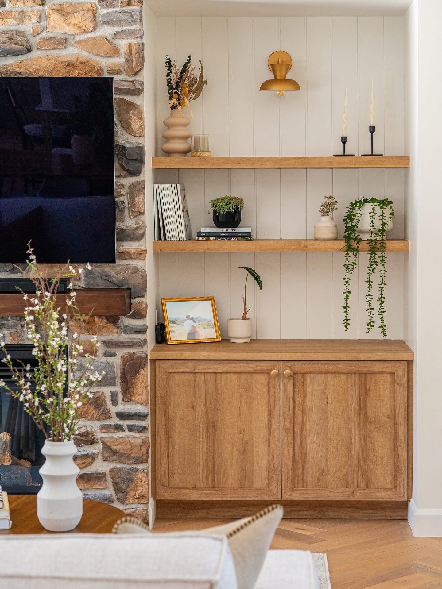 Armoire encastrée en bois avec étagères, plantes et décoration contre un mur blanc, près d'une cheminée en pierre.