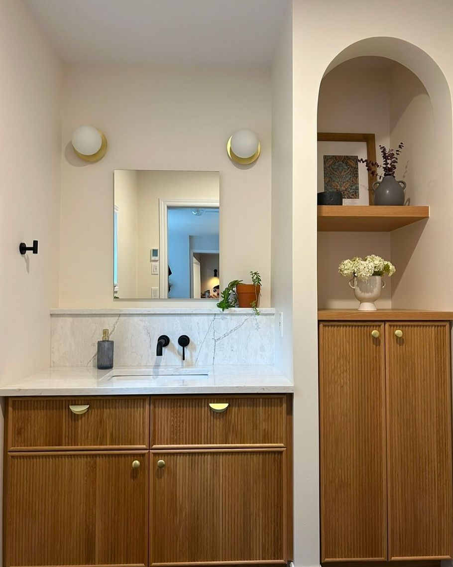Une salle de bain moderne avec des armoires en bois, un comptoir en marbre et une alcôve arquée avec des étagères.