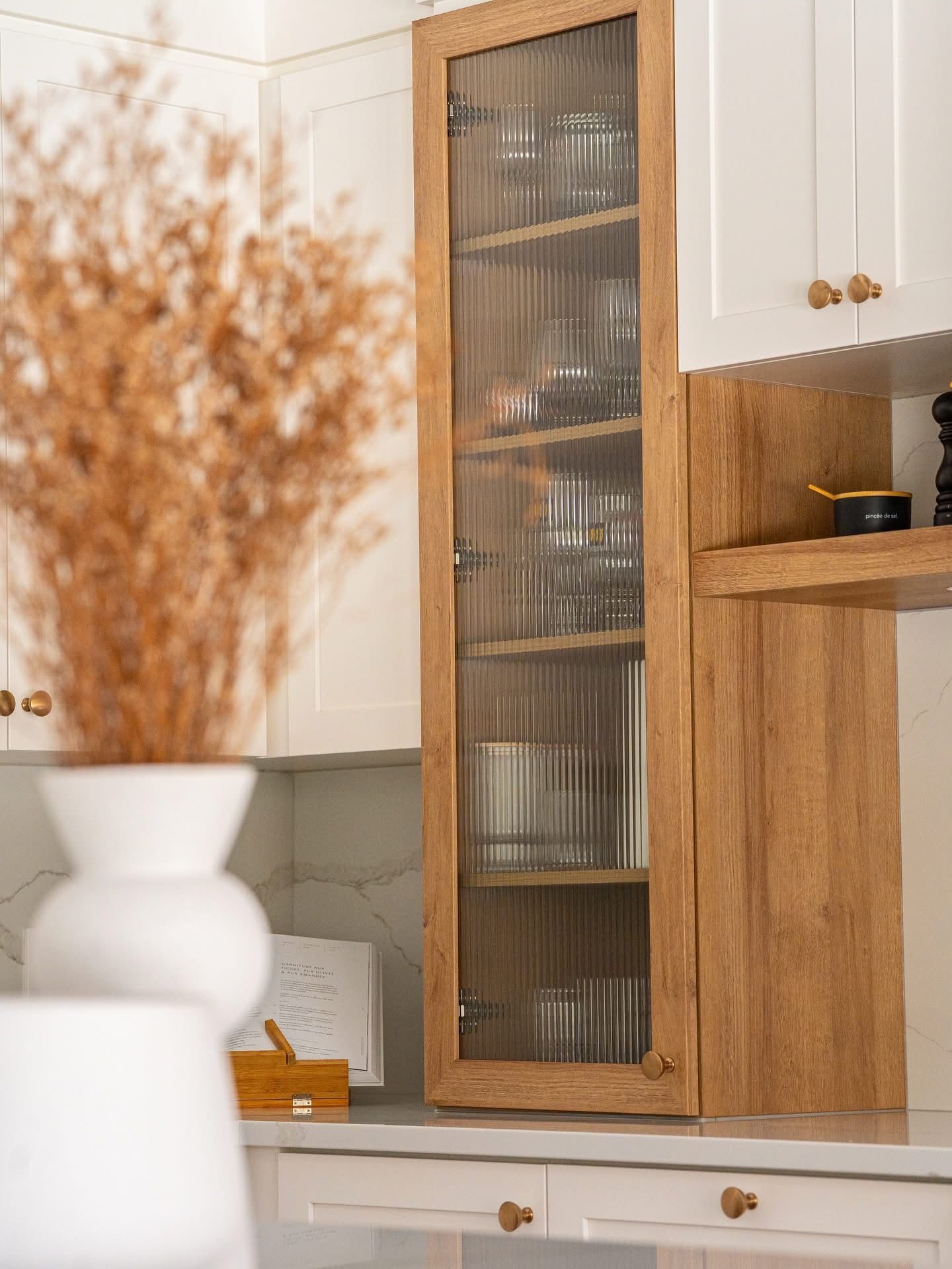 Grande armoire en bois avec porte vitrée contenant de la verrerie, installée dans une cuisine blanche.