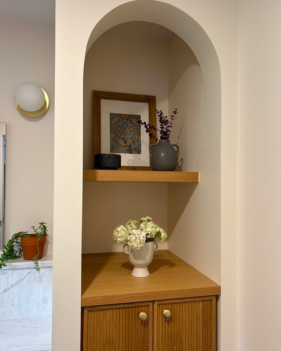 Alcôve arquée intégrée avec armoire en bois, étagère et décor : imprimé encadré, vase et fleurs.