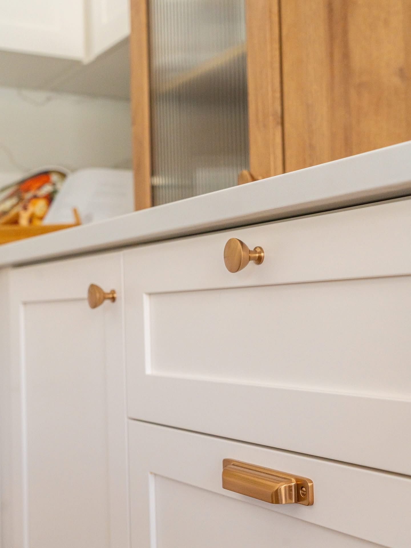 Armoires de cuisine blanches avec quincaillerie dorée. Armoire en bois en arrière-plan.