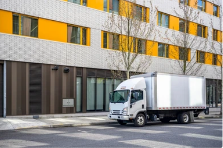 Camion-caisse stationné dans une rue de la ville devant un immeuble à plusieurs étages avec des accents orange et blancs.
