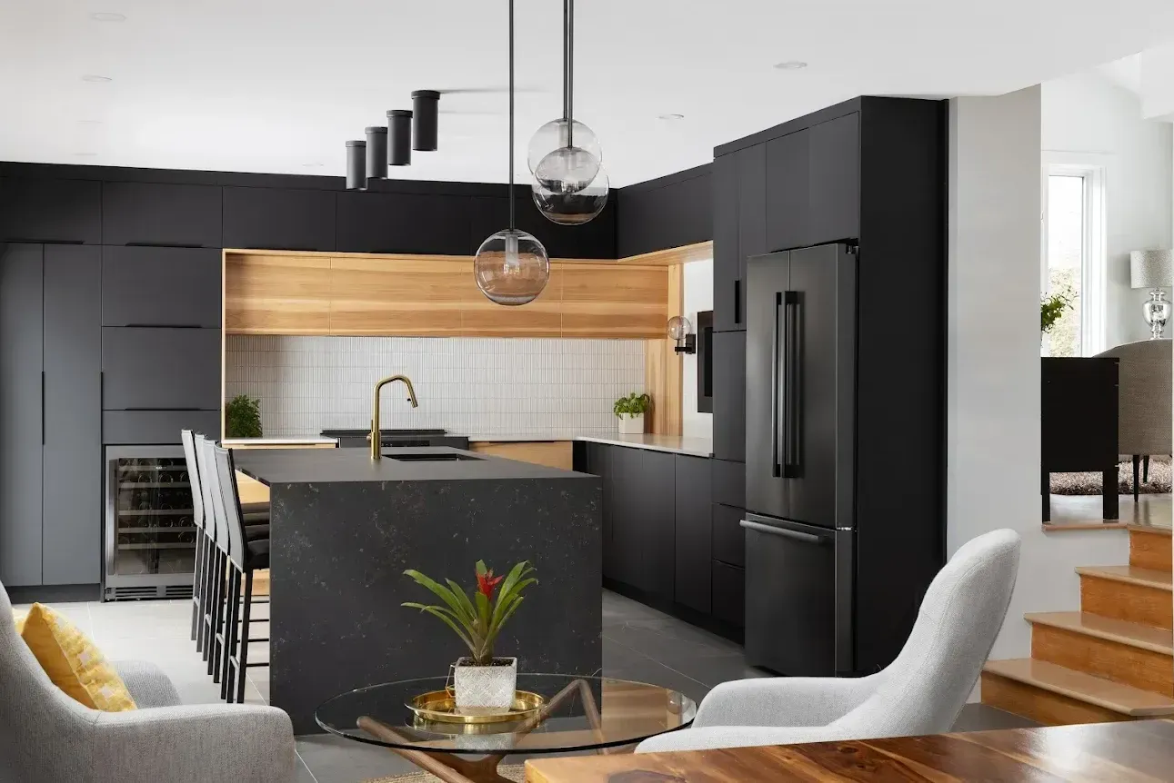 Cuisine moderne avec armoires foncées, îlot et appareils électroménagers noirs.