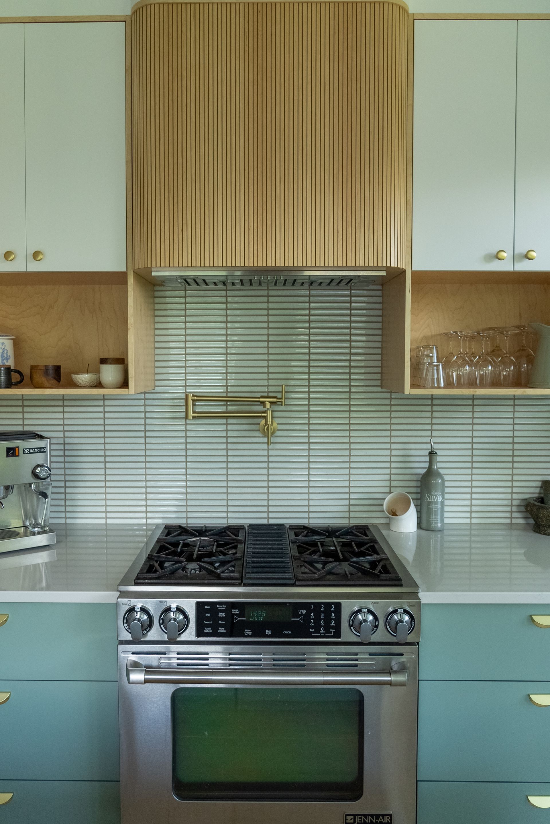 Cuisine avec four et cuisinière en acier inoxydable, armoires bleu sarcelle et accents de bois clair.