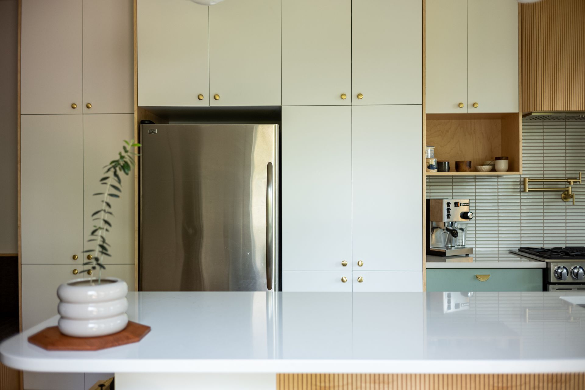 Cuisine moderne avec armoires blanches, réfrigérateur en acier inoxydable et îlot de couleur claire.