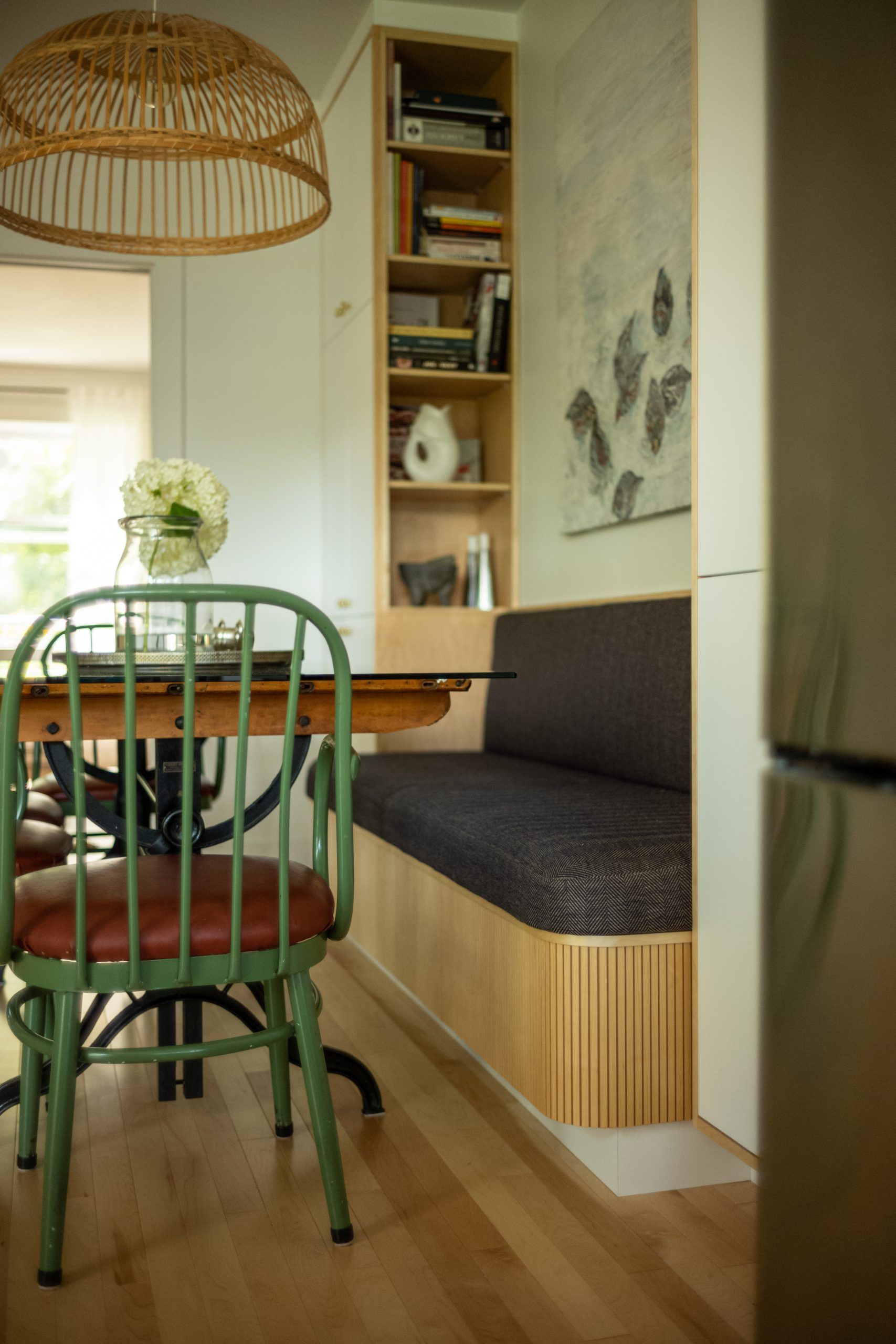 Un petit coin repas avec une chaise verte et un banc intégré. Une étagère et des œuvres d'art sont visibles.